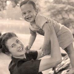 A woman holds a smiling baby in the air as they both look at the camera