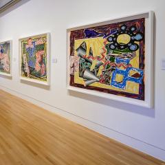 A gallery filled with large, colorful artwork in frames faces a long counter-like display of prints on paper.