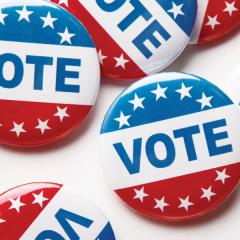 On a white table sits a collection of red, white, and blue buttons with the word Vote and stars printed on them.