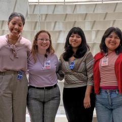 Six young women standing together smiling for a photo in an amphitheater.