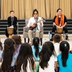 An educator plays the ukulele and two other drum behind her in a school auditorium.