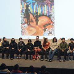 An auditorium watching a discussion on stage with a colorful piece of art on a projector behind them.