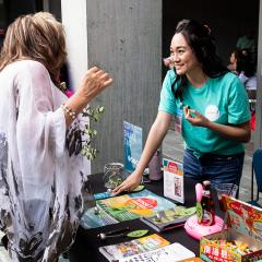 A young intern help a visitor at a table with promotional materials on it.