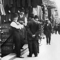 Black and white photograph showing men in suits and bowler hats standing on a street in a city garment district.