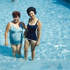 A mid-century photo taken of two women standing in a shallow swimming pool posing for the photo.