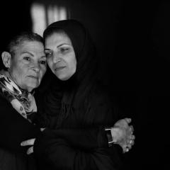 Black and white photograph of two women holding each other with sad, solemn expressions.