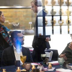 Through a window, people can be seen sitting around a table with a display case reflected above them