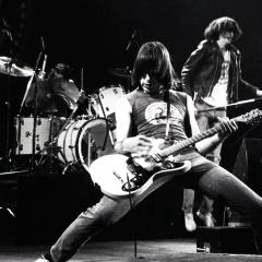 A black and white photo of a guitar player up front from his band on a stage playing.