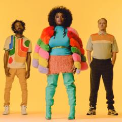 A band with five members pose with colorful outfits.