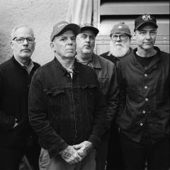 Five men stand close together in black and white, and a man wear sunglasses on stairs.