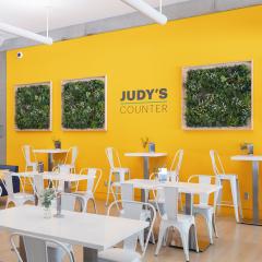 white tables and chairs in front a yellow wall adorned with framed plants