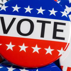A close up of red, white and blue pins that say "vote".