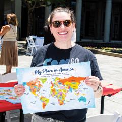A woman hold up a map of the world that reads My Place In America.