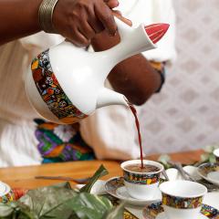 A close up of a person pouring coffee ceremonially in colorfully designed cups.