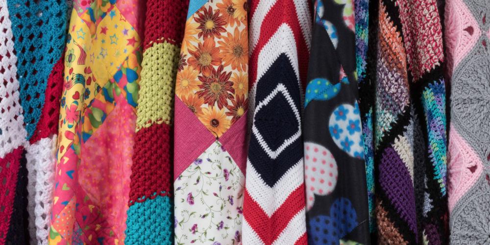 Eight colorful knitted blankets hung next to each other in a row