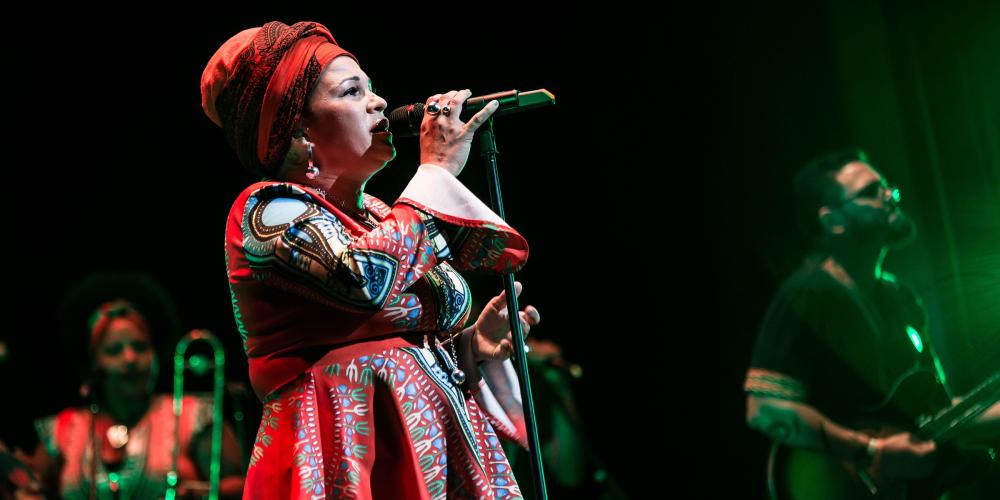 Photograph of Telmary on a dark stage singing into a microphone.
