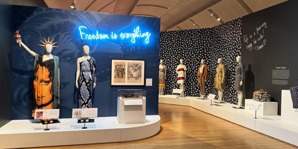 A wide gallery photo showing mannequins in dresses and a neon sign in blue that says Freedom is Everything.