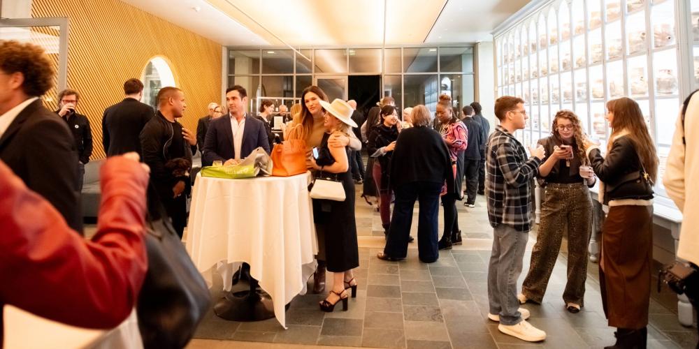 People gather in Ruby Commons at the Skirball talking amongst themselves with refreshments.