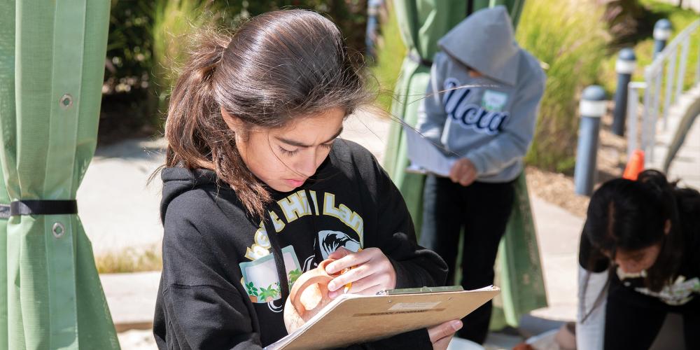 A student digs pottery from a sand box and analyses it.