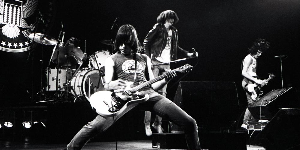 A black and white photo of a guitar player up front from his band on a stage playing.