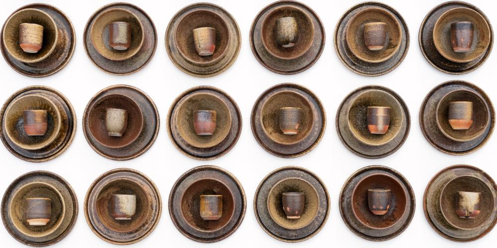 A set of plates, bowls, and cups made from pottery set up in a row.